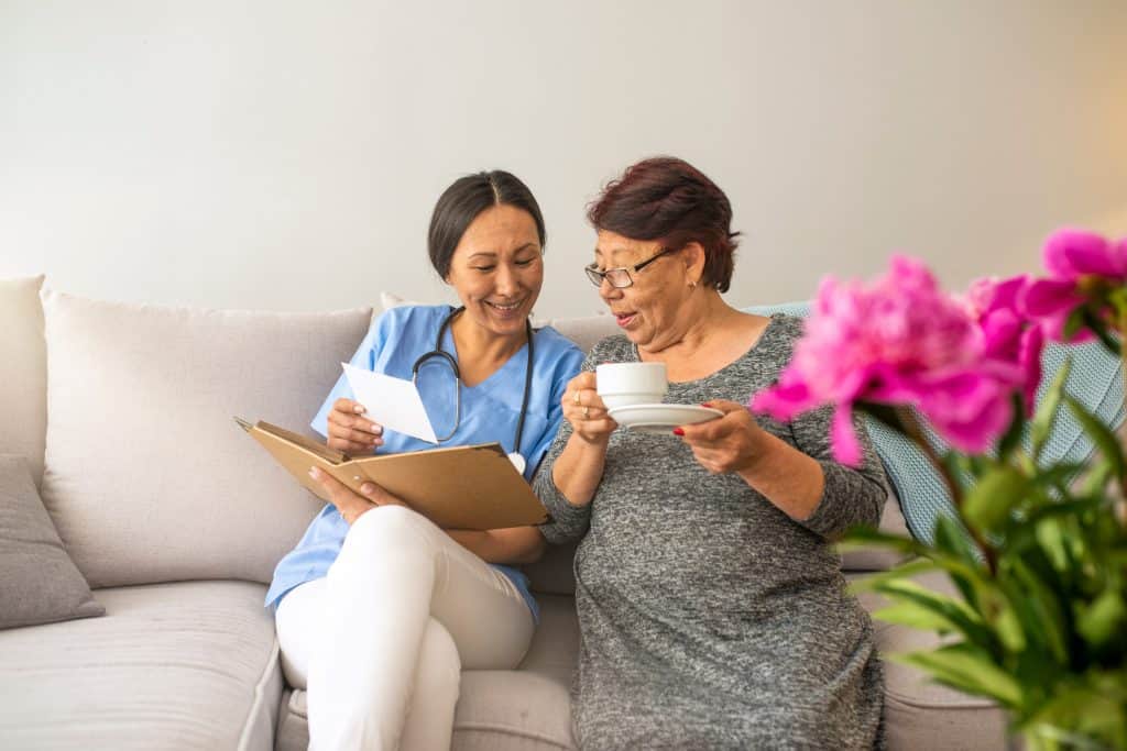 Supportive young nurse looking at elder woman. Smiling beautiful caregiver and disabled old lady at home. Friendly relationship between senior woman and caregiver